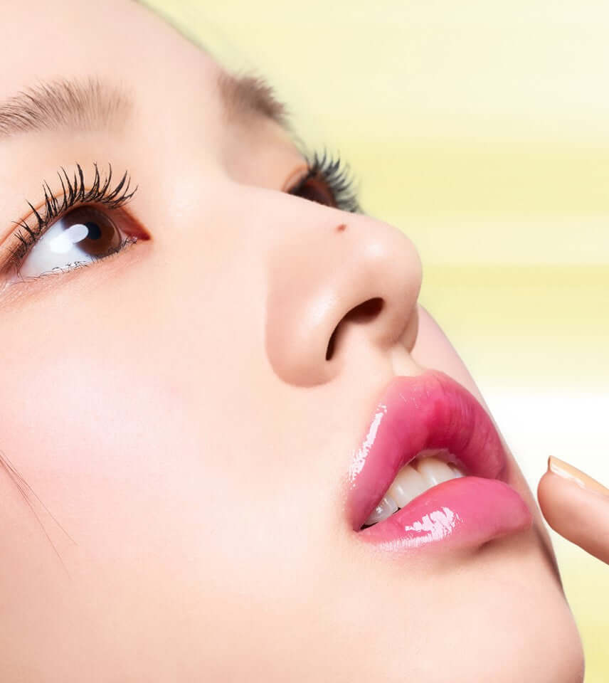 Close-up of a woman's face showcasing glossy lips with pink Laka Bonding Glow Lipstick and beautiful lashes.