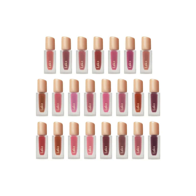 Diverse shades of Laka Fruity Glam Tint lip tints in clear bottles with beige caps, showcasing vibrant, juicy colors.