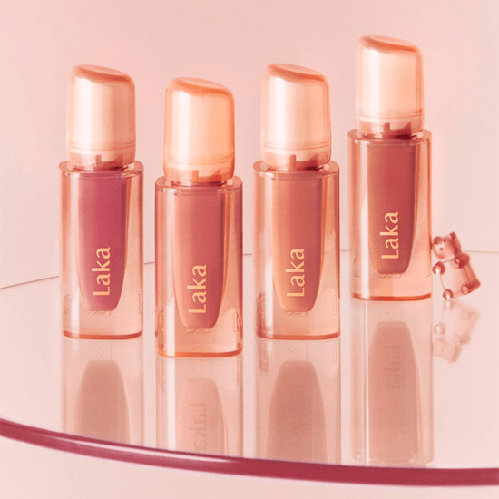 Laka Jelling Nude Gloss bottles displayed on a reflective surface, showcasing four shades of glossy lip tint.