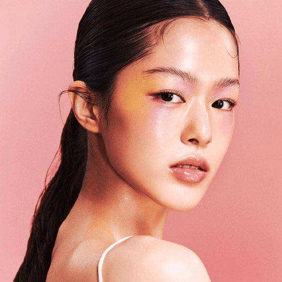 Model showcasing Laka Jelling Nude Gloss with vibrant, glowing makeup and glossy lips against a pink background.