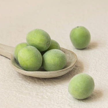 Fresh green plums arranged on a wooden spoon, highlighting their vibrant color and natural texture.